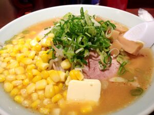 Alt Text: Sapporo Miso Ramen topped with butter, corn, and green onions in a white bowl.