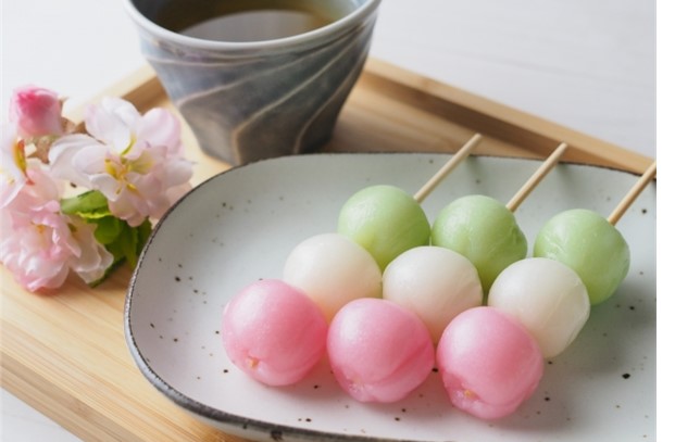 A plate of hanami dango with flowers and a cup of tea on the side