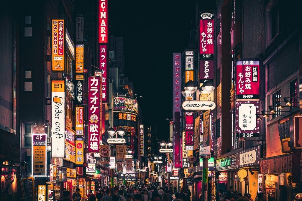 A lively Tokyo city street at night, adorned with a plethora of neon signs, casting a vibrant glow on the bustling urban scene. Photo by Aleksandar Pasaric