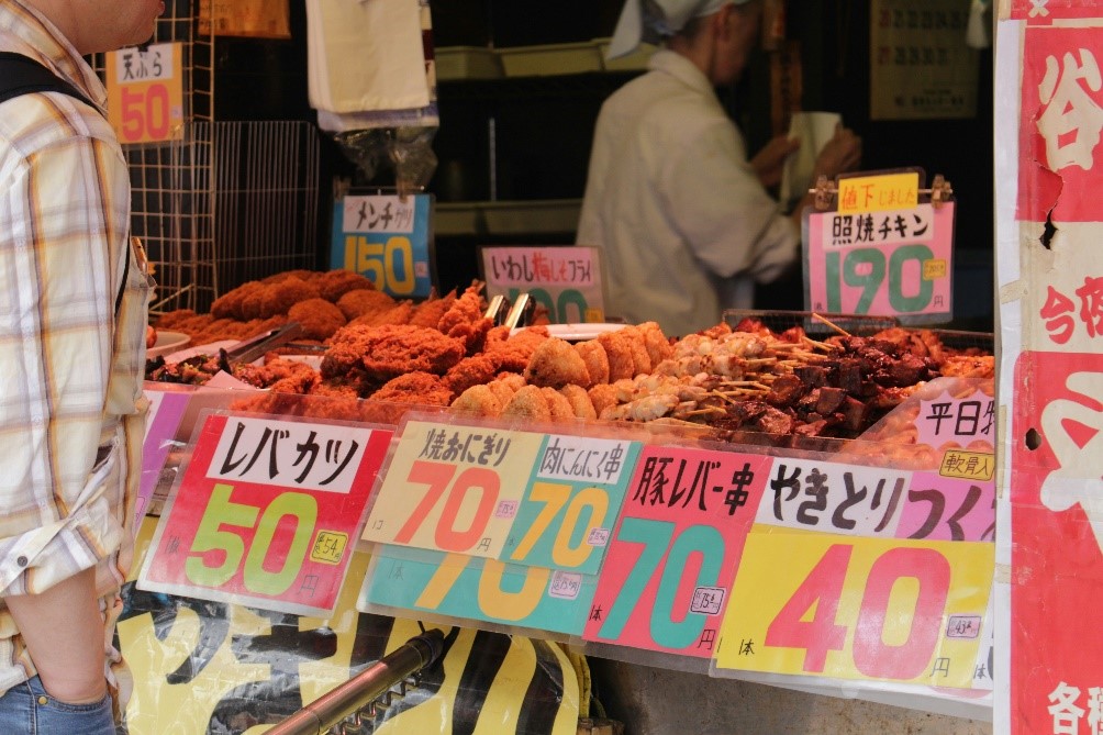 A man standing in front of a display of food at a Tokyo fried food stand.