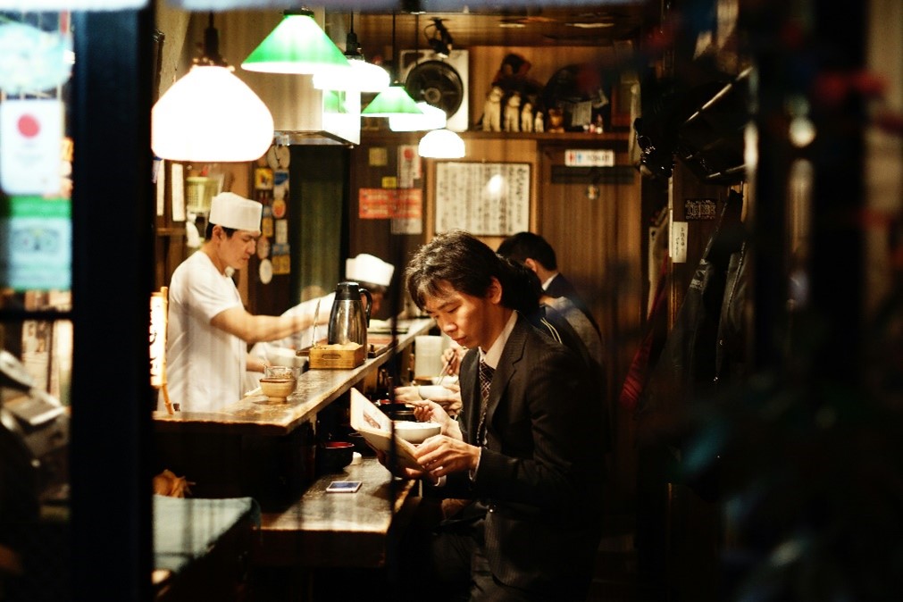 A man sitting at a Tokyo bar, holding a drink in his hand, enjoying a moment of relaxation. 