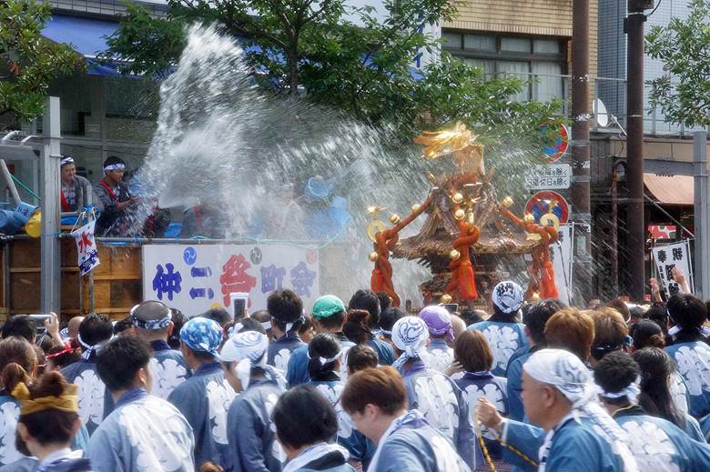 Participants carrying a traditional Japanese mikoshi (portable shrine) while being splashed with water during a lively festival celebration.