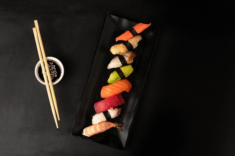 Overhead view of a black rectangular plate holding eight pieces of assorted nigiri sushi
