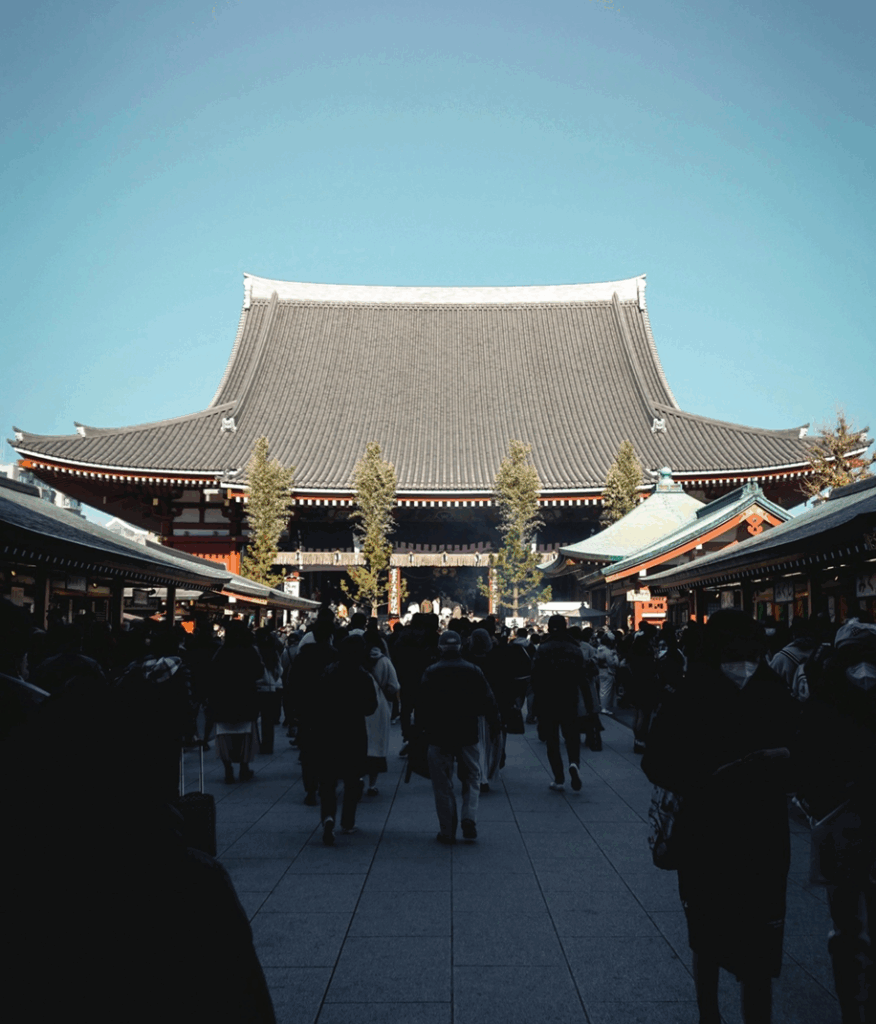 A crowd of people walking toward the large main hall of a traditional Japanese temple