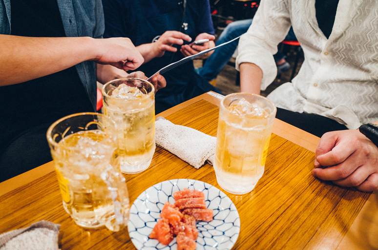 Overhead view of a wooden table at an izakaya with three frosty mugs of iced highball drinks