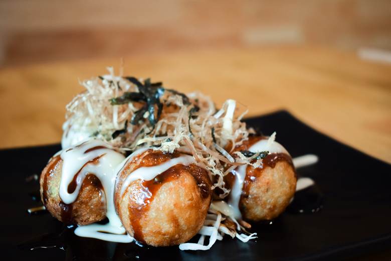 Six golden-brown takoyaki balls on a black plate