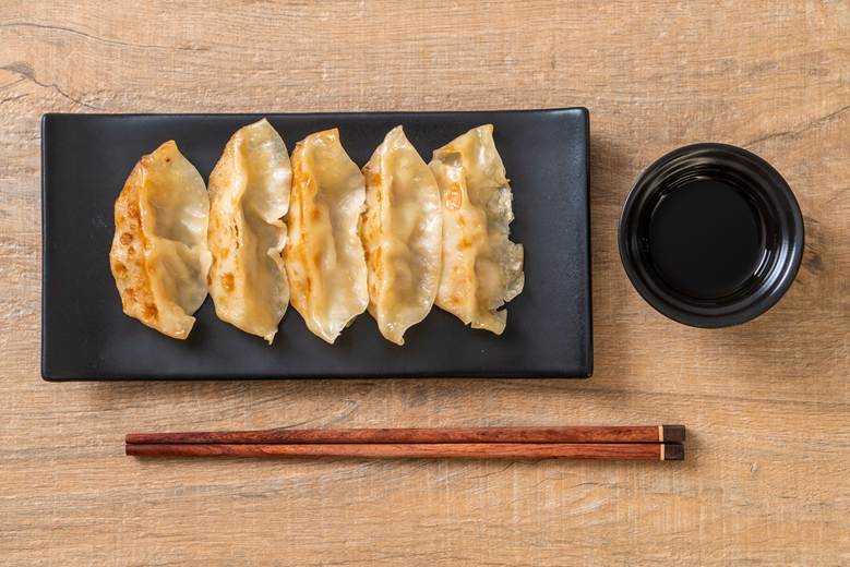 five golden-brown pan-fried gyoza arranged in a row on a black rectangular plate