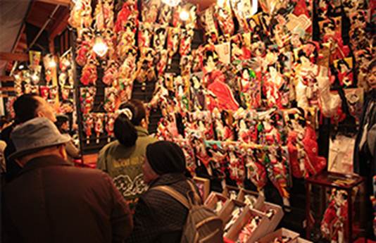 Shoppers browsing a colorful display of traditional Japanese Hagoita paddles at a bustling market stall.