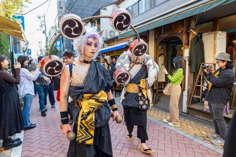 Participants in elaborate costumes walking through a street festival in Tokyo, surrounded by onlookers taking photos.