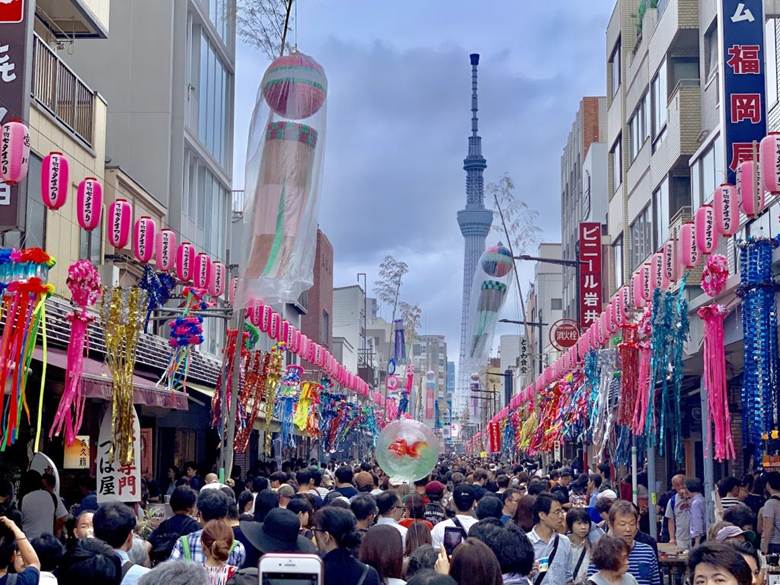 Crowded street festival in Tokyo decorated with colorful lanterns and streamers, with Tokyo Skytree visible in the background.