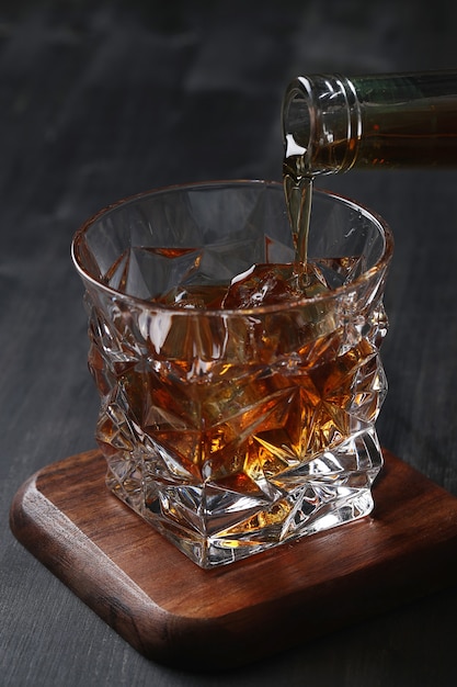 A hand pouring amber liquid from a bottle into a cut crystal whisky glass