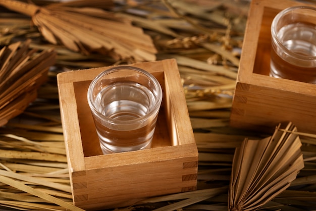 Two glasses of sake in wooden masu cups, surrounded by dried straw and leaves.