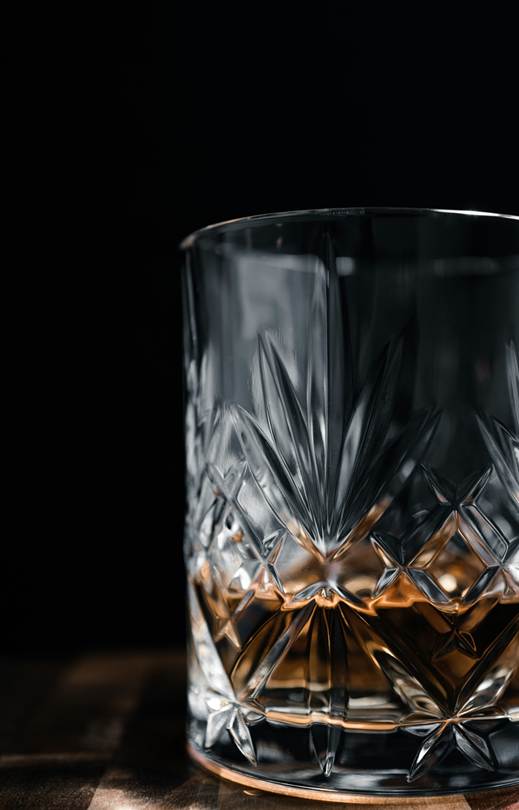 A close-up of a cut crystal whisky glass with amber liquid, set against a dark background.